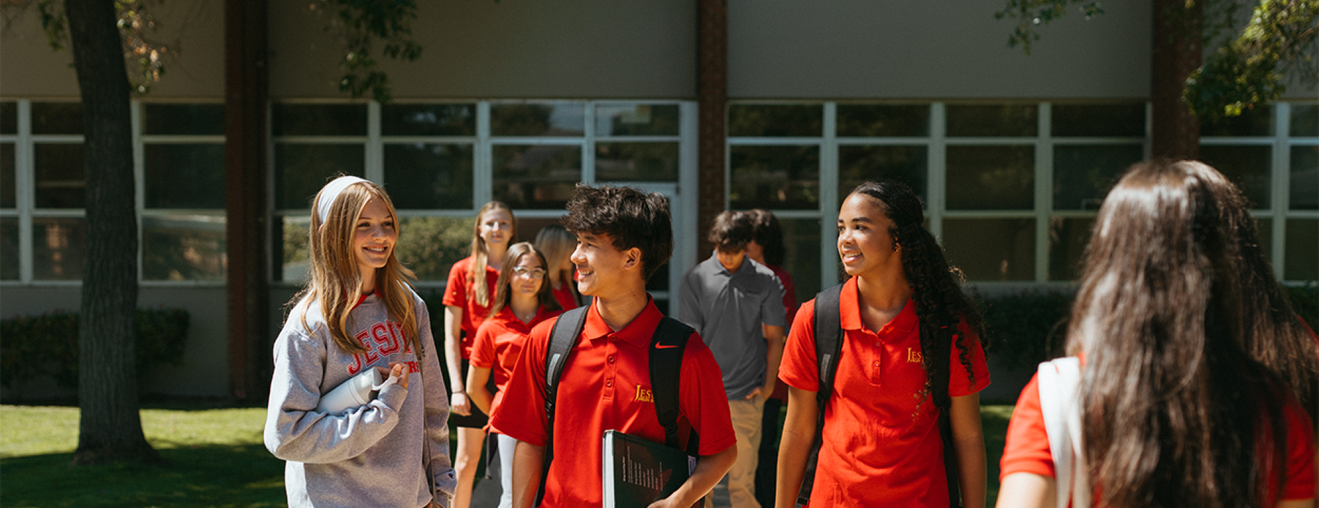 Image of boys and girls with backpacks in Jesuit apparel talking and walking on campus