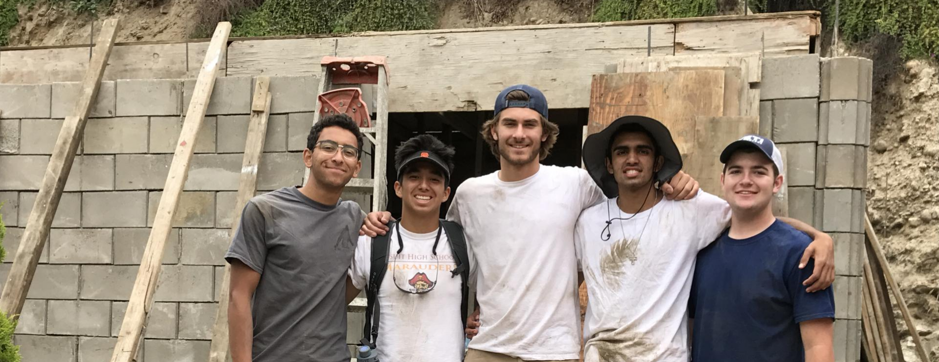Group of 5 students smiling and standing in front of a wall being built in Tijuana Mexico
