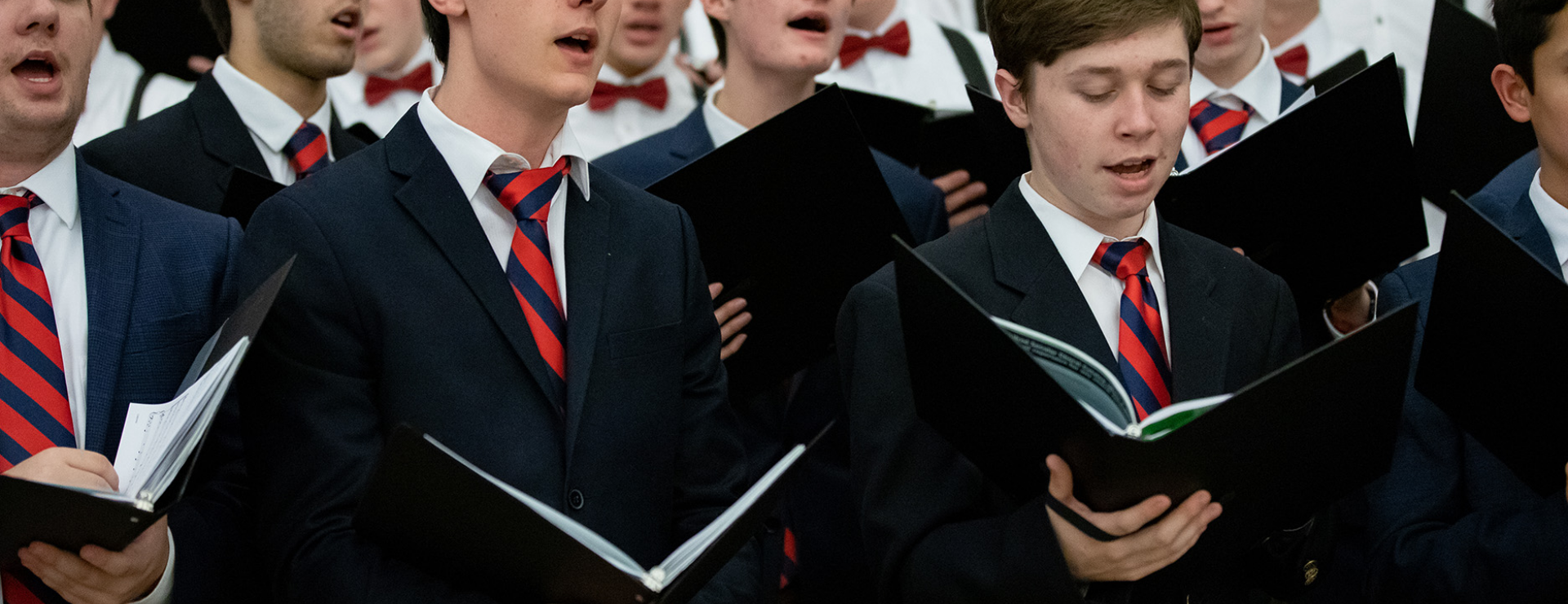 Group of boys singing in suits with red ties at a concert.