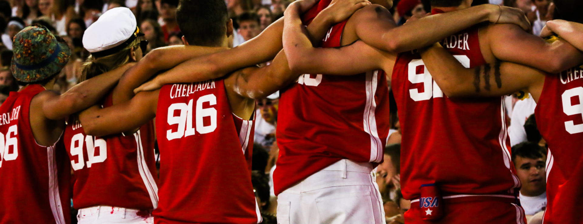 Back of cheerleaders with linked arms at a football game crowd