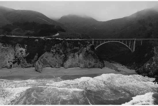 Black and white photo of a bridge near the foggy ocean