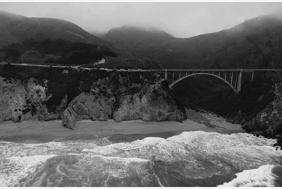 Black and white photo of a bridge near the foggy ocean