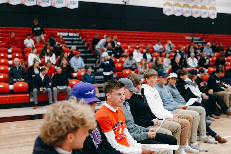 row of student athletes in folding chairs wearing their college sweatshirts 