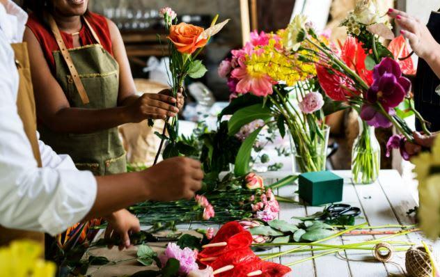 closeup of a table with people's hands arranging bright bunches of flowers