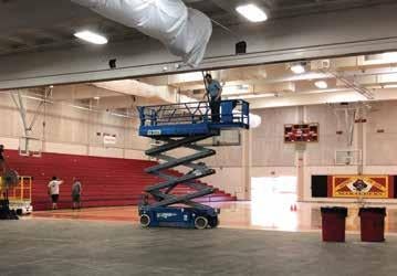 Scissor lift with man working on HVAC in the middle of the gym.