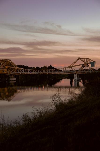 A bridge at the end of sunset, the clouds reflect off the water and the banks are dark