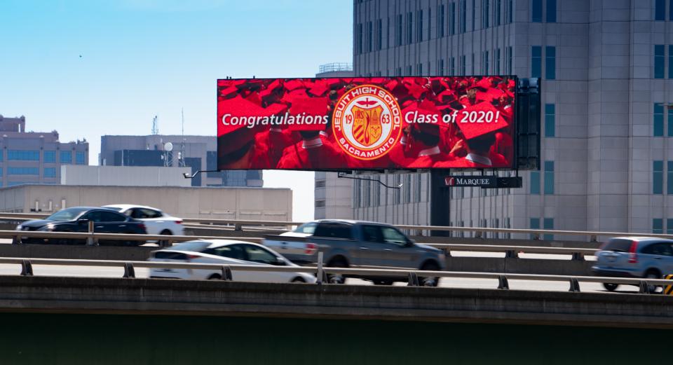 Photo of a digital billboard showing an image of red graduation robes and caps and the jesuit seal with "Congratulations" message