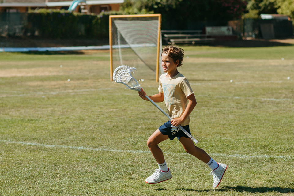 image of young boy running with a lacrosse stick on a field