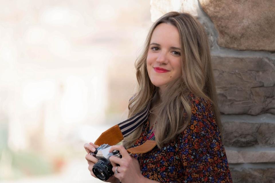 Katie holding a camera and leaning against a brick wall