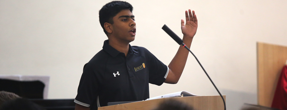 One student with arm slightly upraised in prayer singing at microphone.