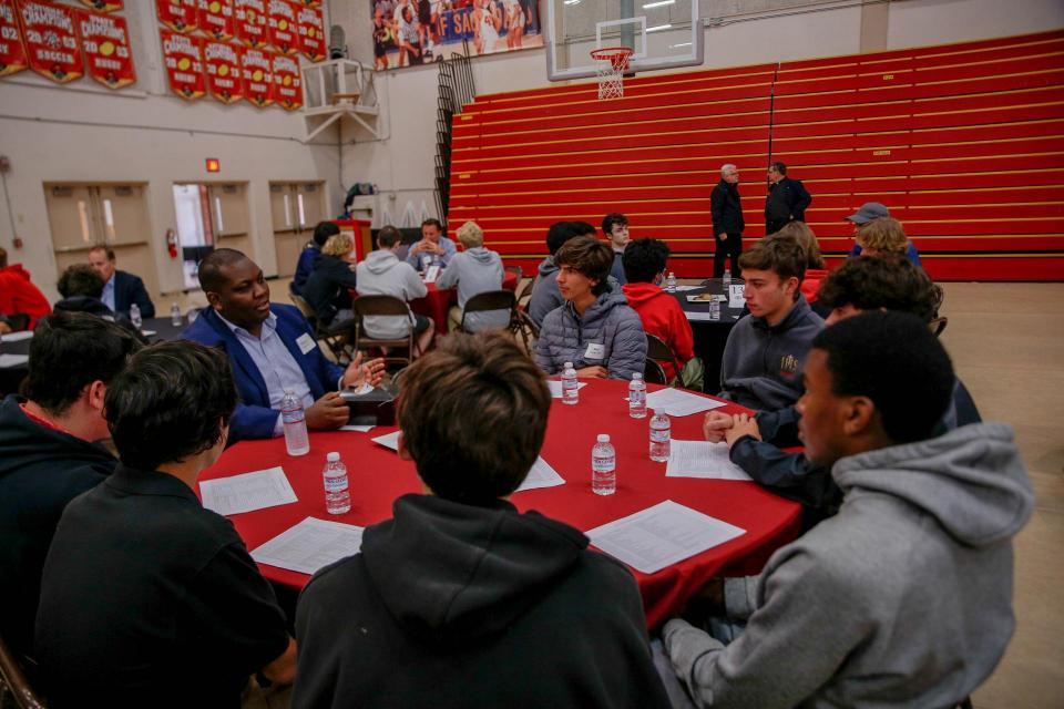 A group of students at a round table with a professional in a suit.