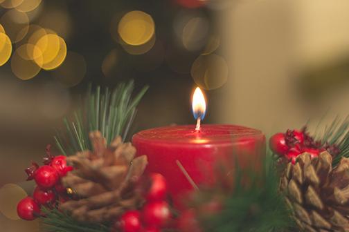 Image of burning candle surrounded by wreath and pinecones