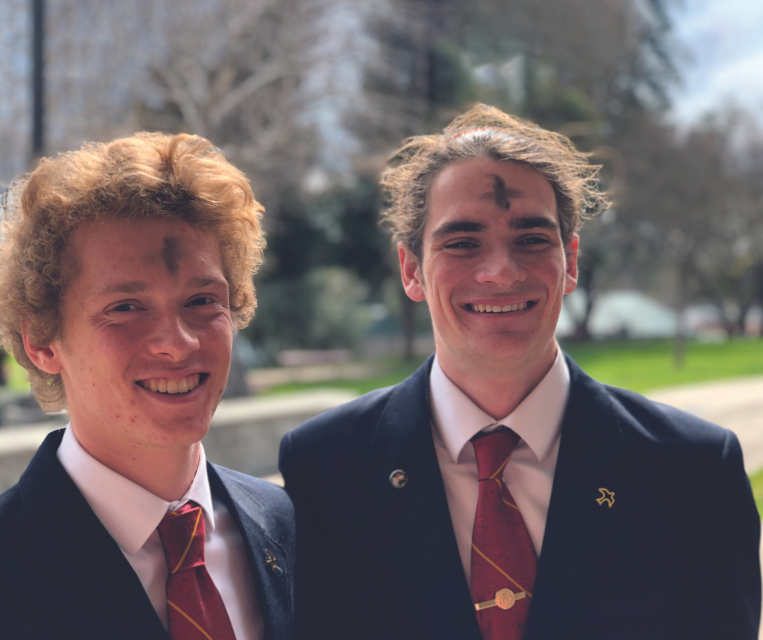 2019 image of two students in liturgy suit and tie, smiling outside on beautiful spring day  with ashes on foreheads