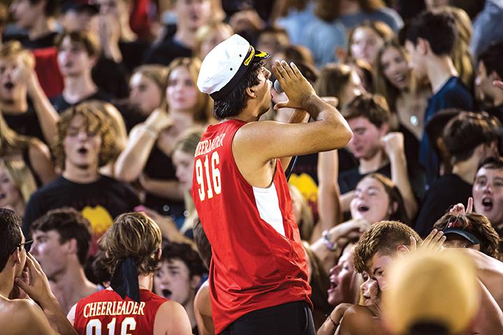 Taj with hands around his mouth, shouting a cheer in front of a crowd.