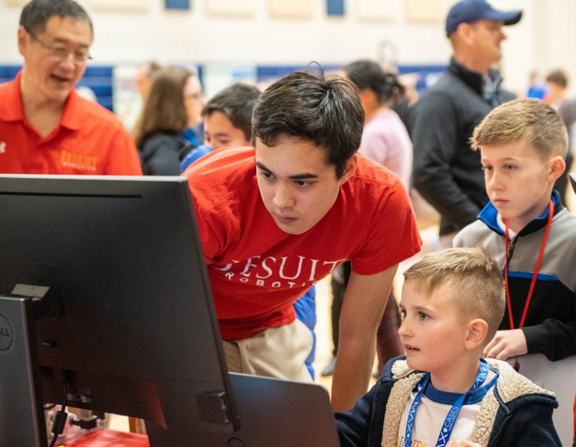 Robotics team member demonstrating movement on computer to young boy