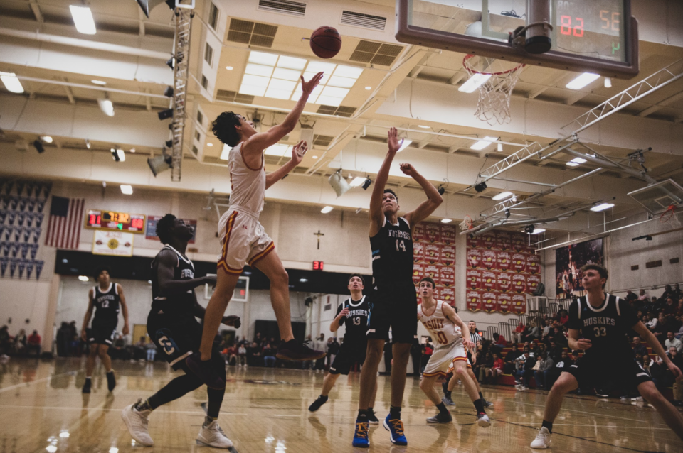 Jesuit player mid air with arms outstretched towards ball and basket.