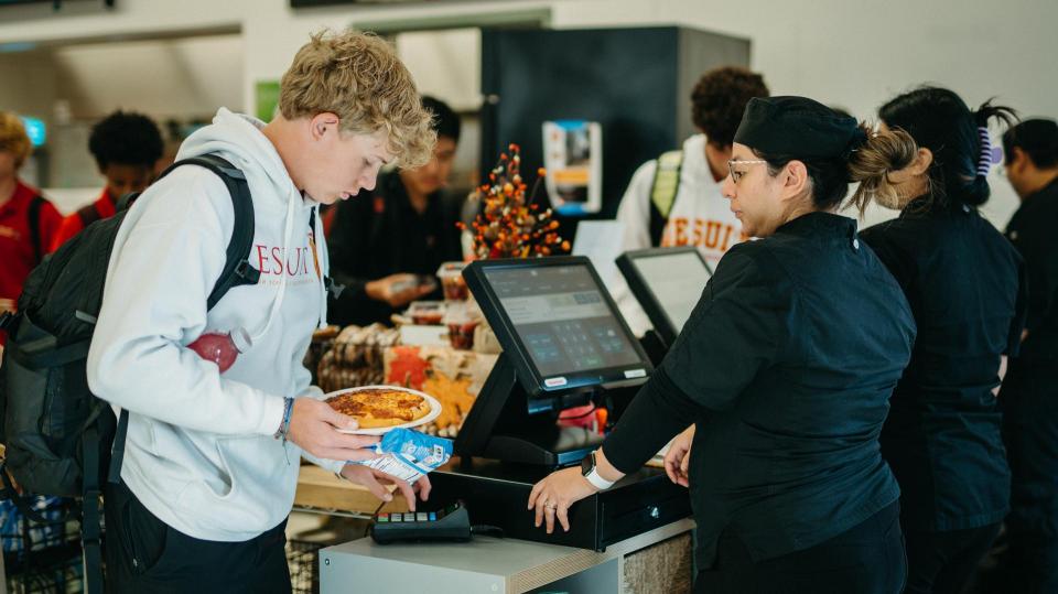 student with food in hand  entering his pin during lunch checkout