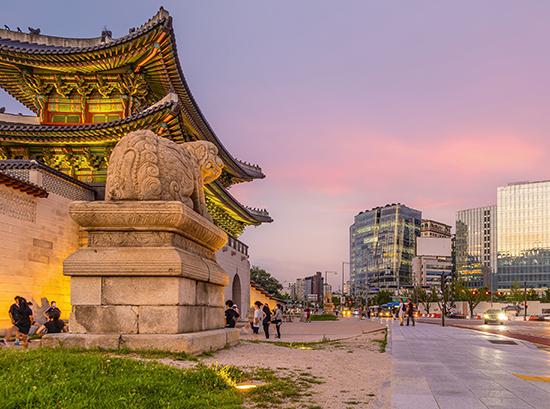 Gyeongbokgung Palace with city in background against pink and purple sky