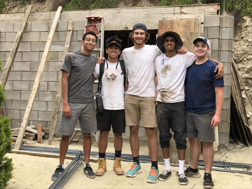 Group of 5 students smiling and standing in front of a wall being built in Tijuana Mexico