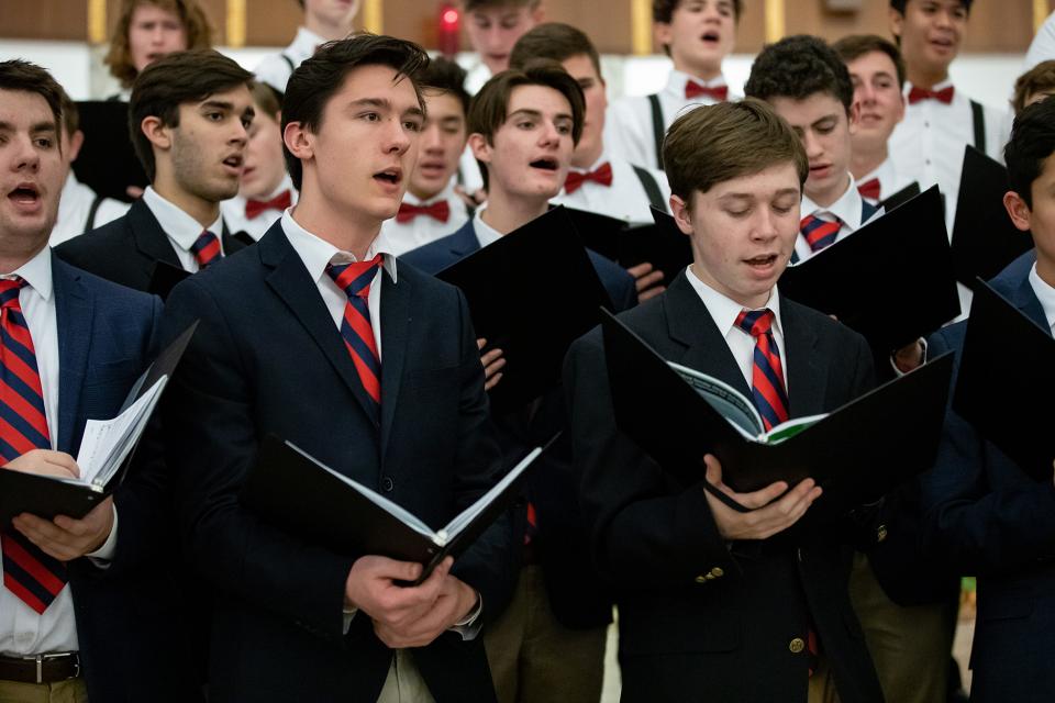 Group of boys singing in suits with red ties at a concert.