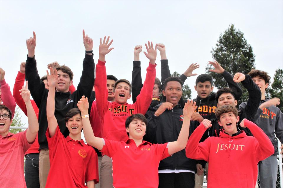 small crowd in stands all in Jesuit logo apparel arms raised high cheering 