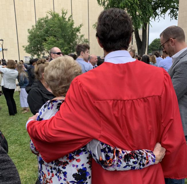 Shot from behind, a grandmother with arm around a graduate in robe