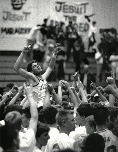 historic black and white photo in the gym with team holding up a player, arms upraised in victory