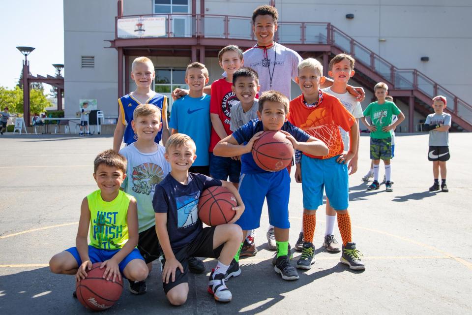 Group of young kids smiling holding a basketball with counselor outside.
