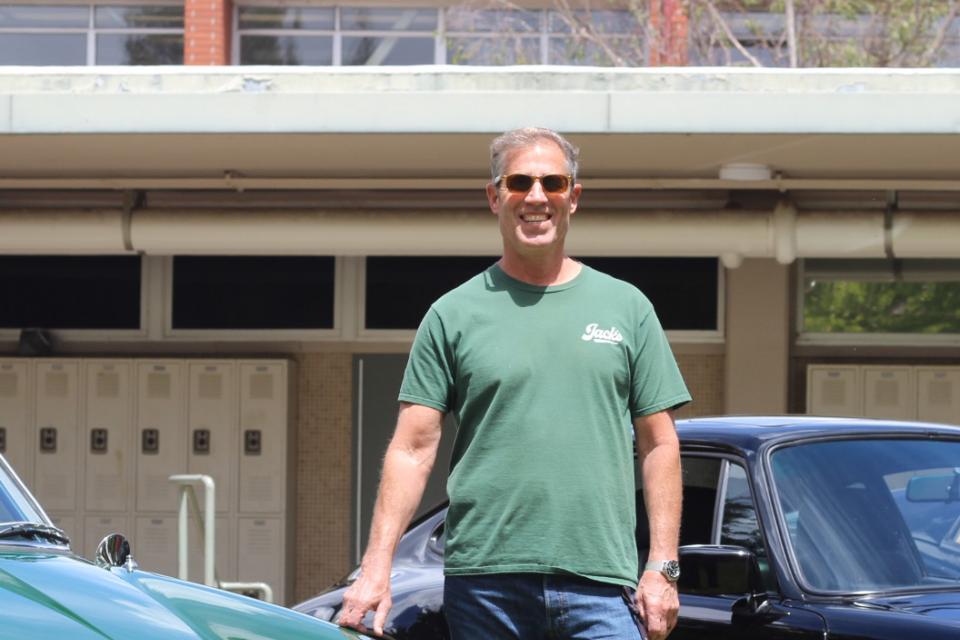 Rose standing between two classic cars in the senior quad