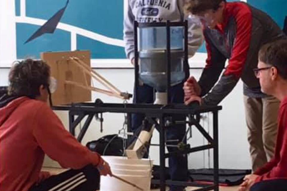 Image of students and instructor standing around a table working on large science project
