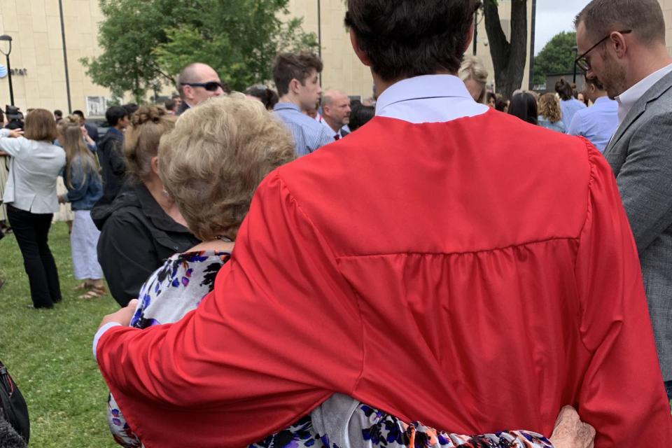 Shot from behind, a grandmother with arm around a graduate in robe