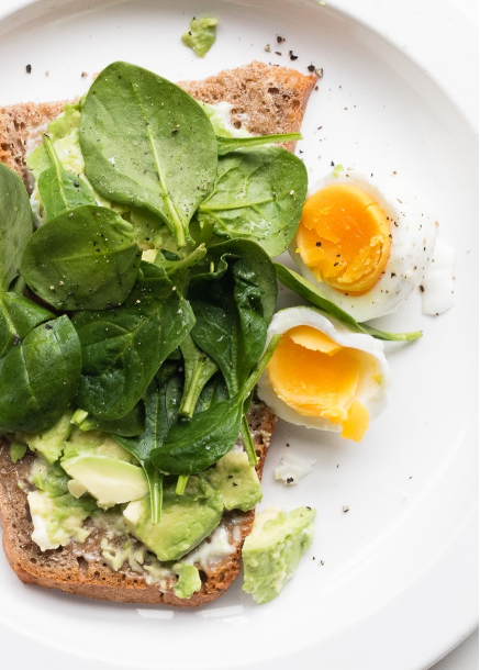 Avocado toast piled with fresh spinach and soft boiled egg