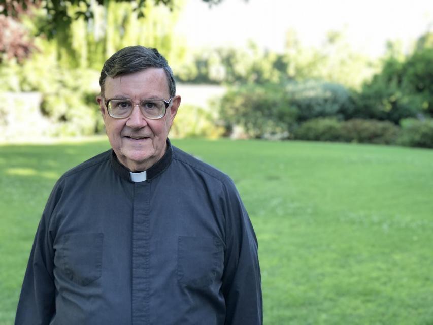 Image of Rev. Harris, S.J. on campus in front of garden