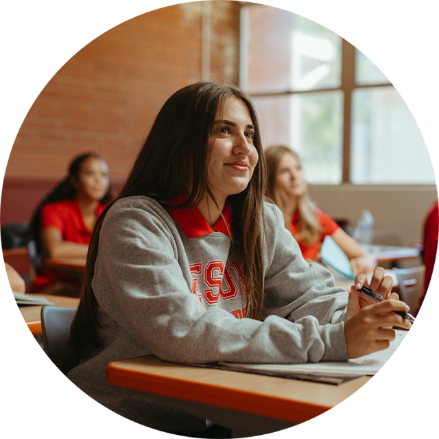 girl in Jesuit sweatshirt smiling at desk in a classroom