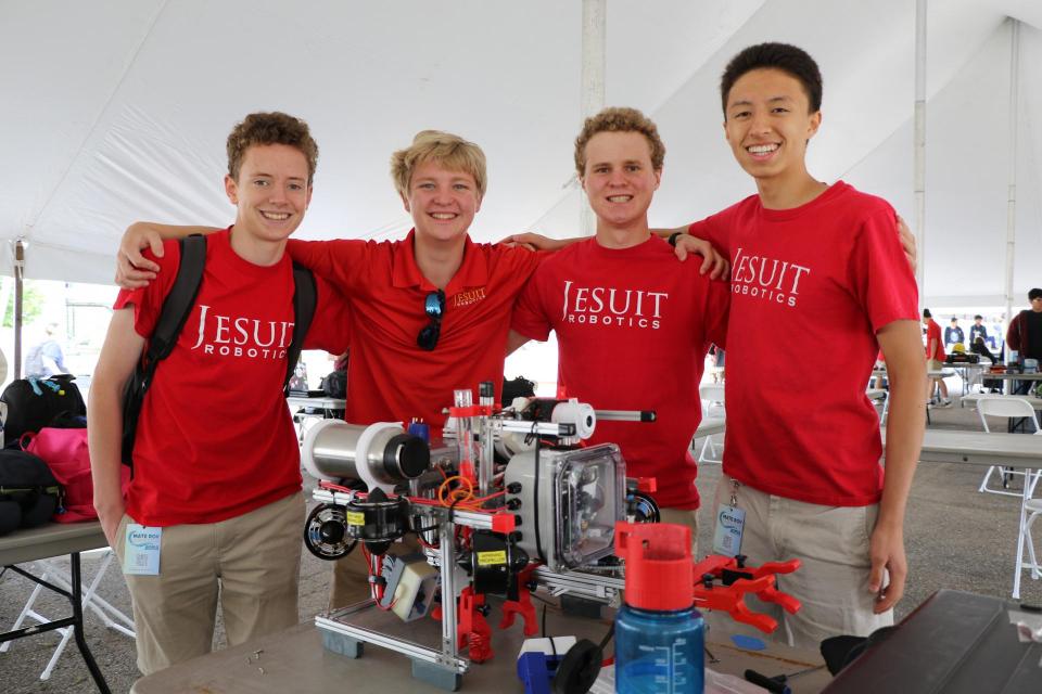 Robotics team at competition smiling with robot under a competition tent