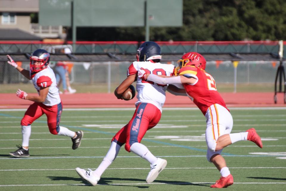 Close up of Jesuit player with arms around a Pleasant Grove player who is carrying the ball.