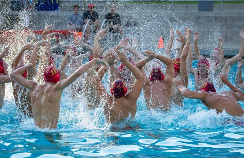 Team in the water with arms upraised mid-cheer, water splashing.