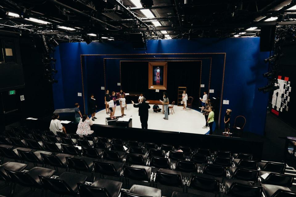 Image of empty theater with a few campers on the stage practicing