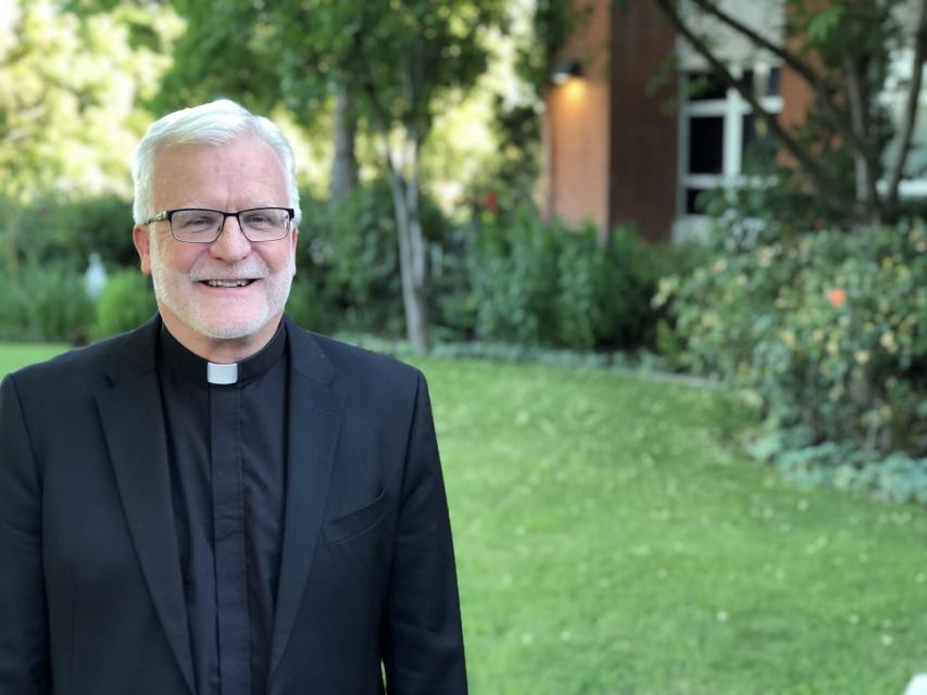 Image of Rev. John P. McGarry, S.J. on campus in front of garden
